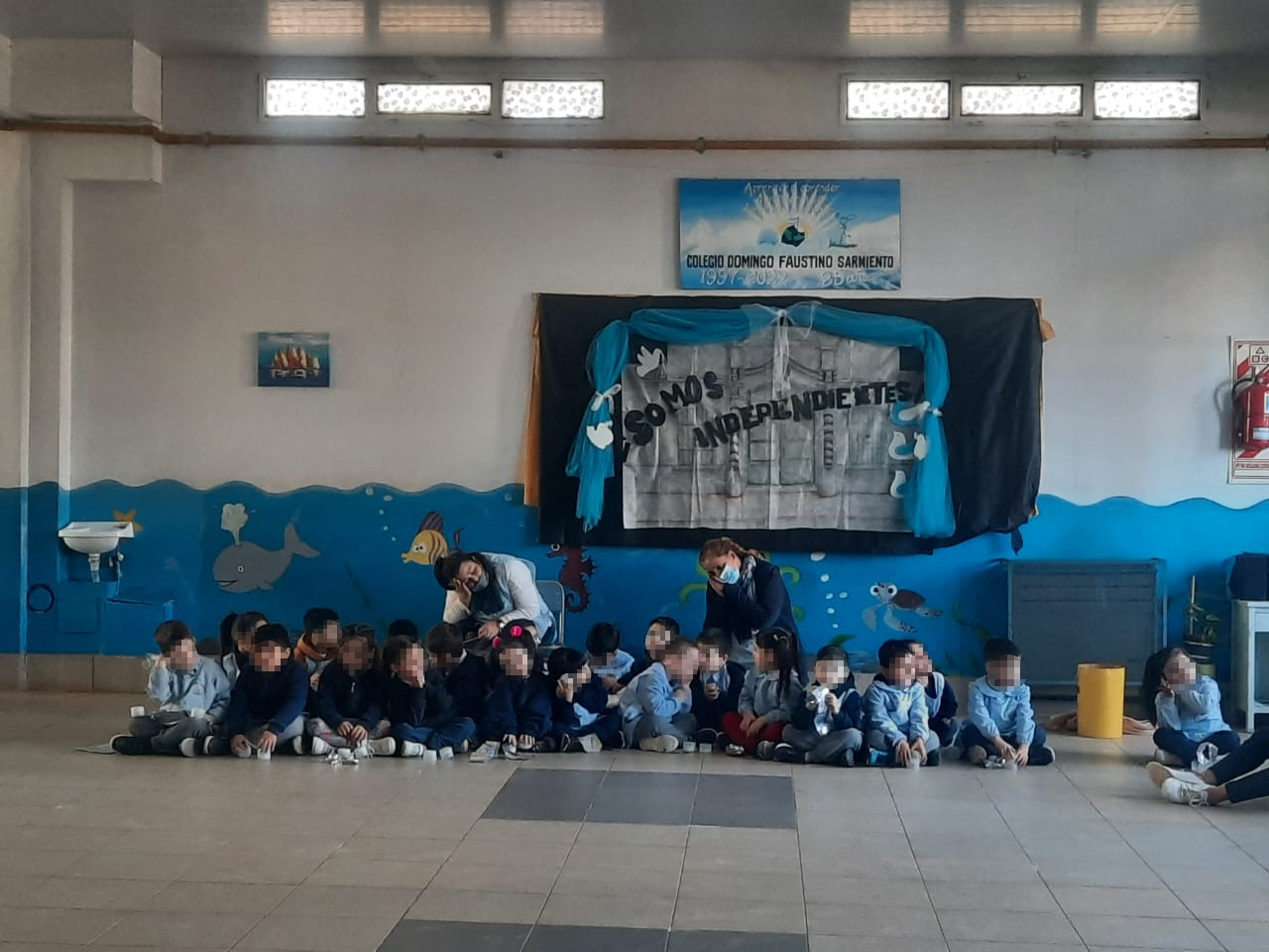 Grupo de estudiantes y personas adultas reunidos en el salón del colegio